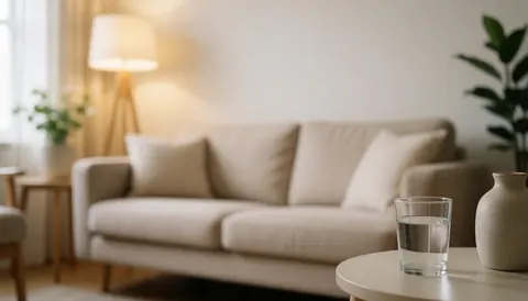 Arrière-plan chaleureux et flou d'un salon avec canapé beige, lampe, table, verre d'eau et vase, idéal pour ajouter du texte.