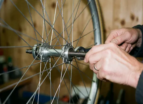 Gros plan sur des mains utilisant une clé pour serrer l'écrou d'une roue de vélo dans un atelier avec murs en bois et détails métalliques brillants.