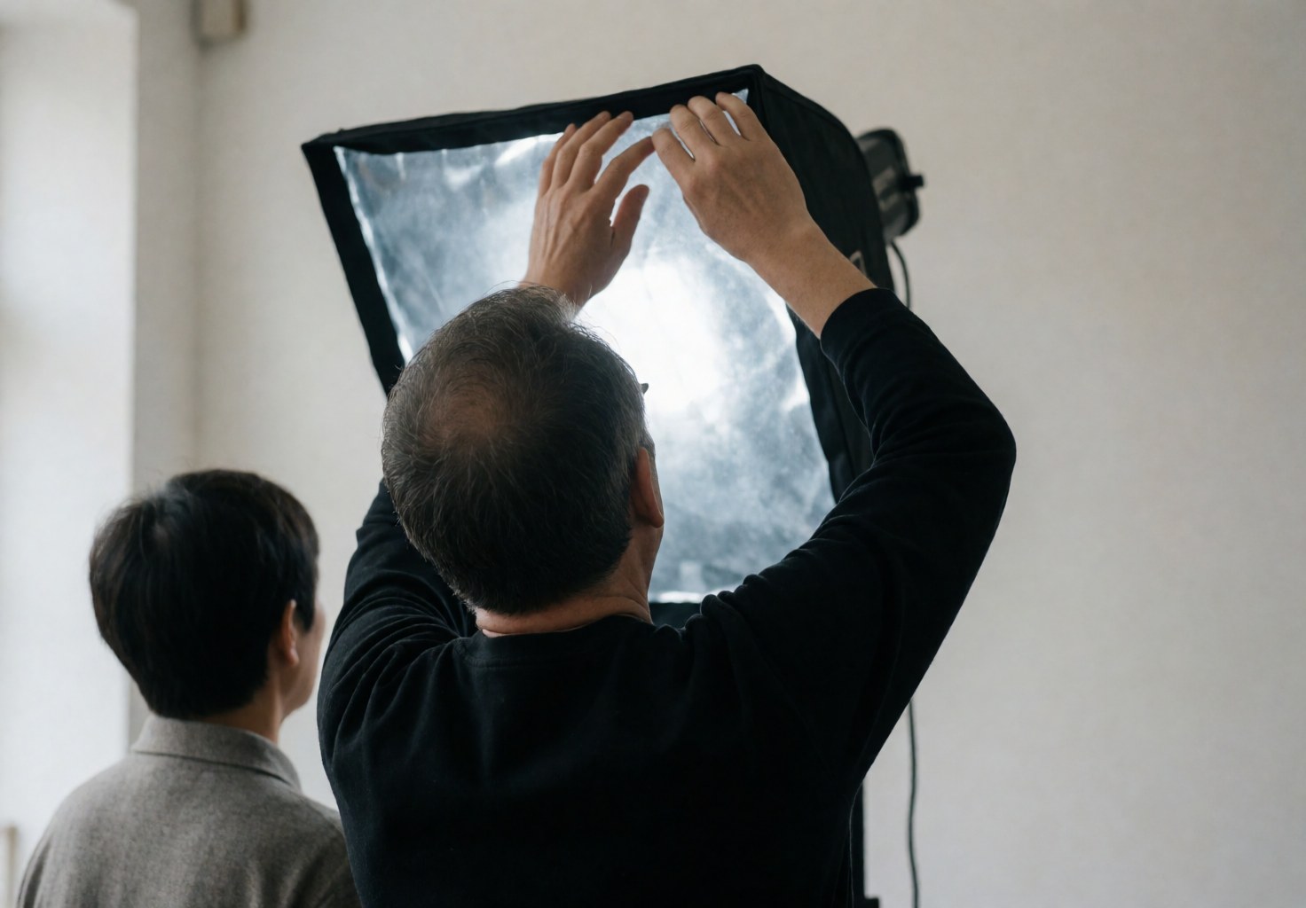 Un vidéaste professionnel ajuste un softbox de lumière dans un studio blanc, tandis qu'une autre personne observe le travail.