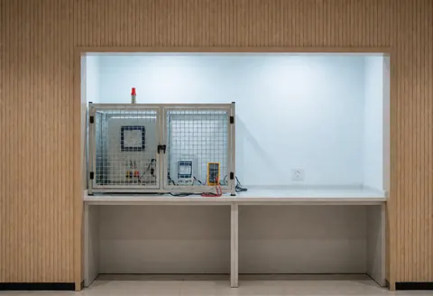 Zone de test pour micro-ondes équipée d'une boîte de sécurité, de compteurs et de murs en bois clair, offrant un espace propre et prêt pour la vérification technique.