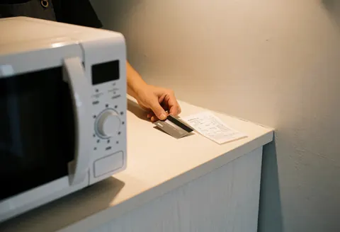 Une main adulte pose une carte de crédit sur un comptoir à côté d'un reçu, avec un microonde blanc réparé en premier plan.