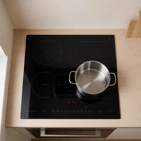 Cuisinière à induction noire avec casserole en acier inoxydable vide sur un plan de travail en bois clair, murs beige, vue de dessus.