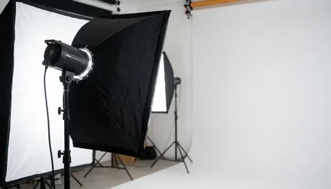 Studio de tournage professionnel doté d'un softbox, d'un fond blanc courbe et d'équipements lumineux en premier plan, idéal pour les vidéographes.