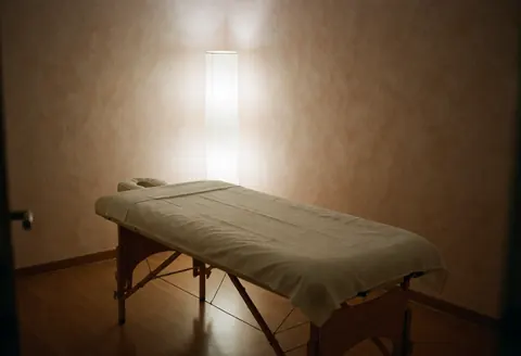 Pièce de massage équipée d'une table de traitement, aux murs en terre cuite et à l'éclairage doux de lampe, créant une ambiance calme et propre.