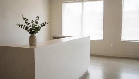 Réception minimaliste de clinique avec table blanche, plante en pot et fenêtres laissant entrer la lumière naturelle, créant une ambiance sereine et propre.