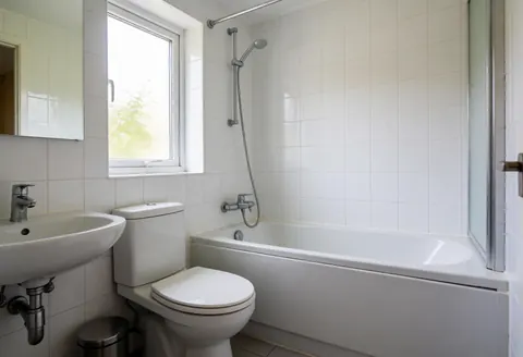 Salle de bain résidentielle propre avec toilettes, lavabo et baignoire, éclairée par une fenêtre, idéale pour les plombiers.