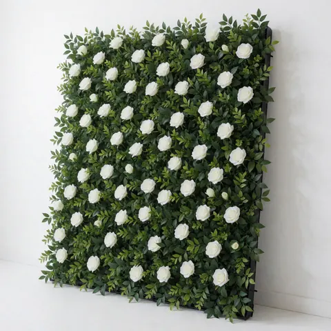 Panneau décoratif modulaire pour événements composé de roses blanches et de feuillage vert, idéal pour les fonds et la décoration, fixé sur un mur blanc, vu en angle.