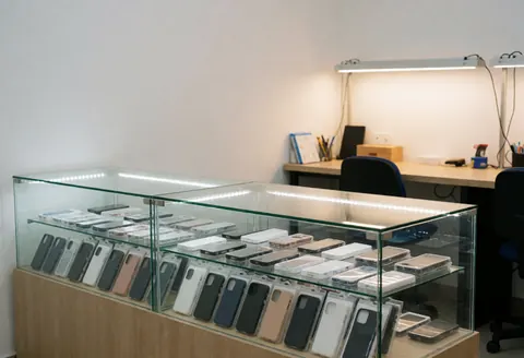 Magasin de réparation de téléphones avec vitrine éclairée présentant des coques et protecteurs d'écran, produits en vente dans un environnement propre et professionnel.