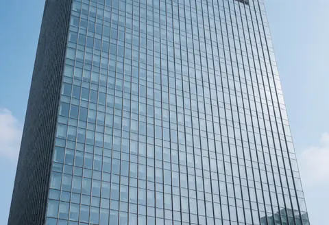 Façade d'un bâtiment moderne avec de nombreuses fenêtres en verre reflétant le ciel bleu, idéale pour illustrer les services de nettoyage de vitres.