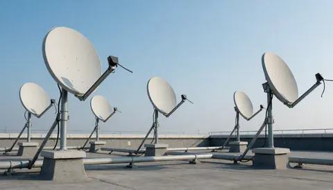 Plusieurs antennes paraboliques montées sur un toit en béton avec des tuyaux, sous un ciel bleu clair, idéal pour les entreprises d'installation.