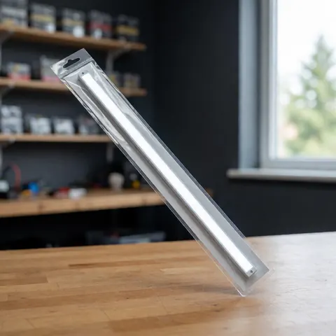 Kit de lumière LED dans son emballage transparent posé sur une table en bois avec des étagères de composants électroniques floues en arrière-plan et lumière naturelle.