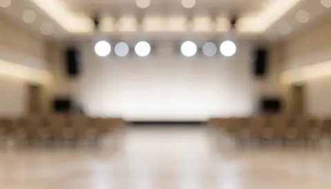 Arrière-plan d'événement professionnel avec des lumières de scène et des sièges flous, idéal pour ajouter du texte dans un environnement chaleureux et professionnel.