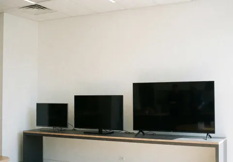 Trois téléviseurs de tailles différentes posés sur un comptoir moderne avec des murs blancs, créant un environnement propre et professionnel pour une boutique de réparation.