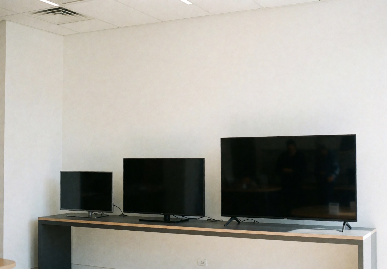 Trois téléviseurs de tailles différentes posés sur un comptoir moderne avec des murs blancs, créant un environnement propre et professionnel pour une boutique de réparation.
