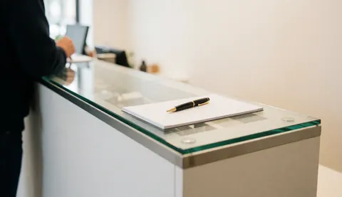 Bureau de réception moderne avec un stylo et un carnet posés dessus, idéal pour la bijouterie ou la reloquinerie, sur fond flou avec des murs clairs.