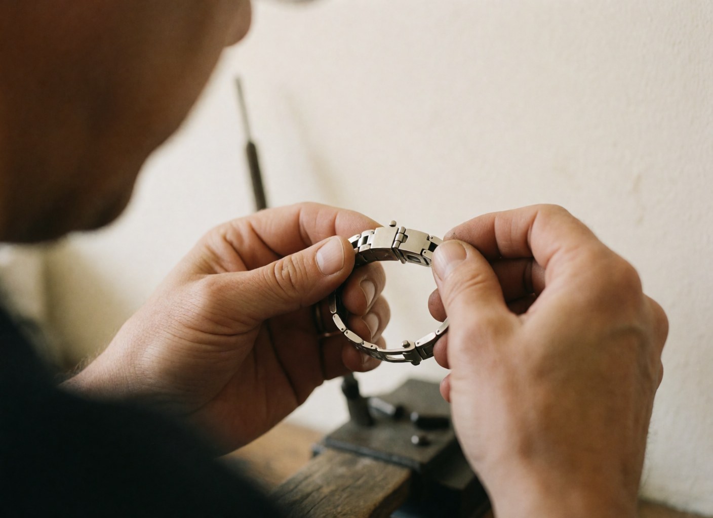 Mains d'un technicien ajustant avec précision une fermeture de montre en métal brillant sur un fond de atelier flou aux murs clairs.