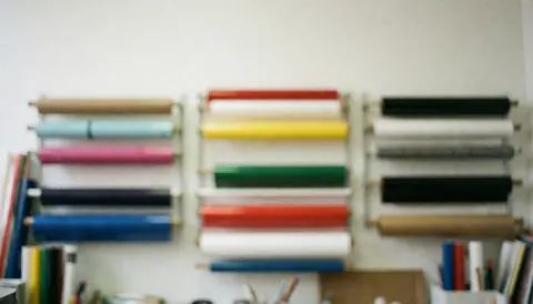 Arrière-plan flou d'un atelier de sérigraphie avec des étagères contenant des rouleaux de vinyle aux couleurs vives, idéal pour superposer du texte publicitaire.