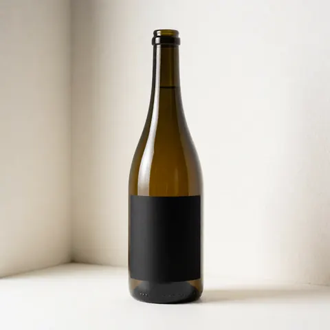 Bouteille en verre posée dans un coin blanc, éclairée par une lumière douce, idéale pour présenter un design d'étiquette personnalisé.