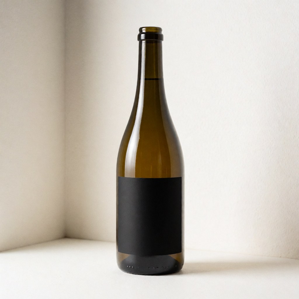 Bouteille en verre posée dans un coin blanc, éclairée par une lumière douce, idéale pour présenter un design d'étiquette personnalisé.