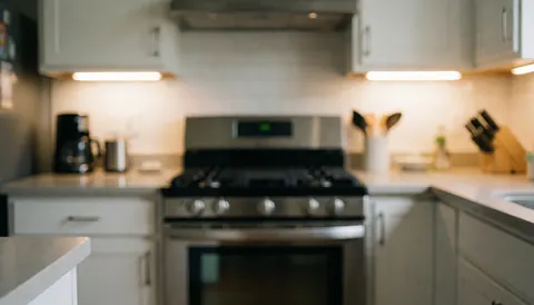 Cuisine moderne avec cuisinière à gaz et armoires blanches, éclairage chaleureux, fond flou pour textes, idéal pour services de réparation de cuisines.