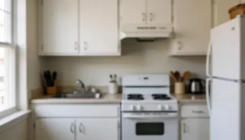 Cuisine compacte équipée d'une cuisinière, d'un réfrigérateur et de placards blancs sur un fond doux et flou, idéal pour illustrer des services de réparation.