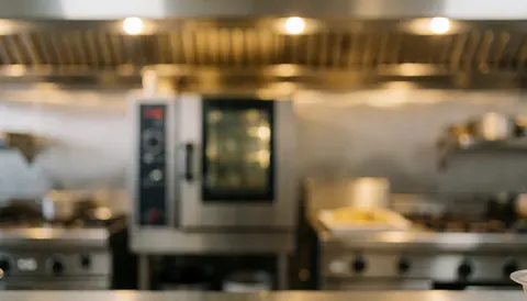Arrière-plan flou d'une cuisine commerciale équipée de fours en acier inoxydable et d'un système de ventilation, éclairage chaud pour superposer du texte.