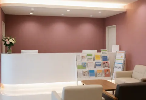 Réception d'un centre éducatif avec un comptoir blanc, un mur rose, des chaises et des brochures pour étudiants, éclairage chaleureux et accueillant.