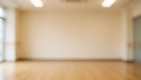 Arrière-plan d'un studio de danse aux murs beige et au sol en bois, éclairage chaleureux, idéal pour textes ou logos, sans personnes ni détails reconnaissables.