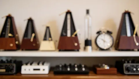 Étagère en bois dans un studio de musique contenant des métronomes, des horloges et des accessoires, sur fond flou chaud pour texte sur le rythme et la discipline.