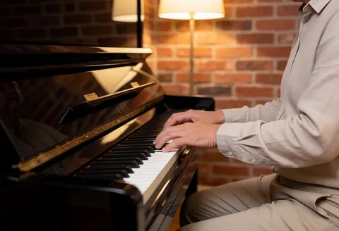 Professionnel jouant du piano dans un studio avec un mur de briques, des lumières chaudes et les mains sur les touches.
