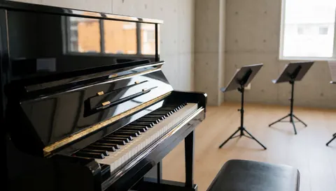 Piano à queue noir avec touches visibles, sol en bois clair et pupitres dans un studio aux murs de béton.