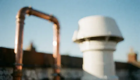 Vue floue d'une terrasse avec des tuyaux en cuivre et un conduit blanc sous un ciel bleu clair, servant de fond pour du texte commercial.