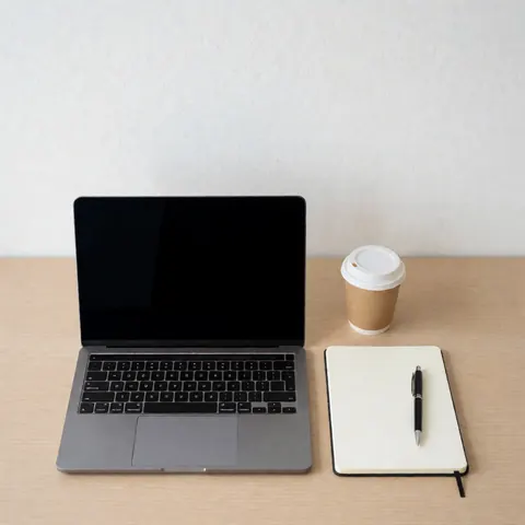 Vue aérienne d'un bureau ordonné avec un ordinateur portable éteint, un cahier blanc et une tasse de café, idéal pour étudier ou suivre des cours de programmation.