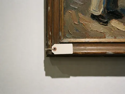 Gros plan sur un tableau en peinture à l'huile en relief, son cadre en bois et une étiquette blanche suspendue. Idéal pour les galeries d'art ou les boutiques.