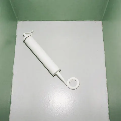 Tube de silicone blanc non appliqué posé sur une surface grise lisse avec des murs verts en arrière-plan, éclairage uniforme et propre, idéal pour les installateurs de fenêtres isolantes.