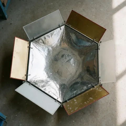 Réflecteur photographique à cinq panneaux avec surfaces argentées, dorées et blanches posé sur un sol en béton éclairé par la lumière naturelle.