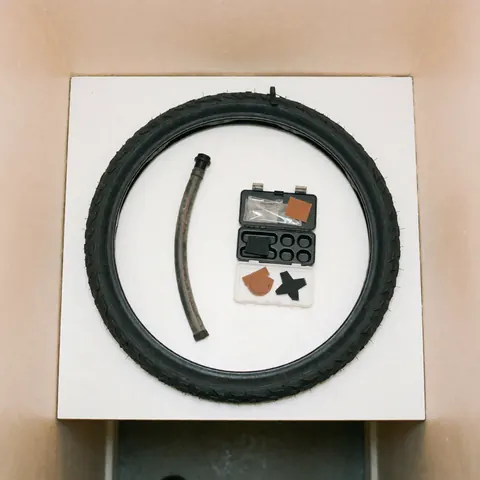 Pneu de vélo neuf accompagné d'un kit de réparation comprenant des patches et des outils sur fond blanc, idéal pour un atelier de bicyclettes.