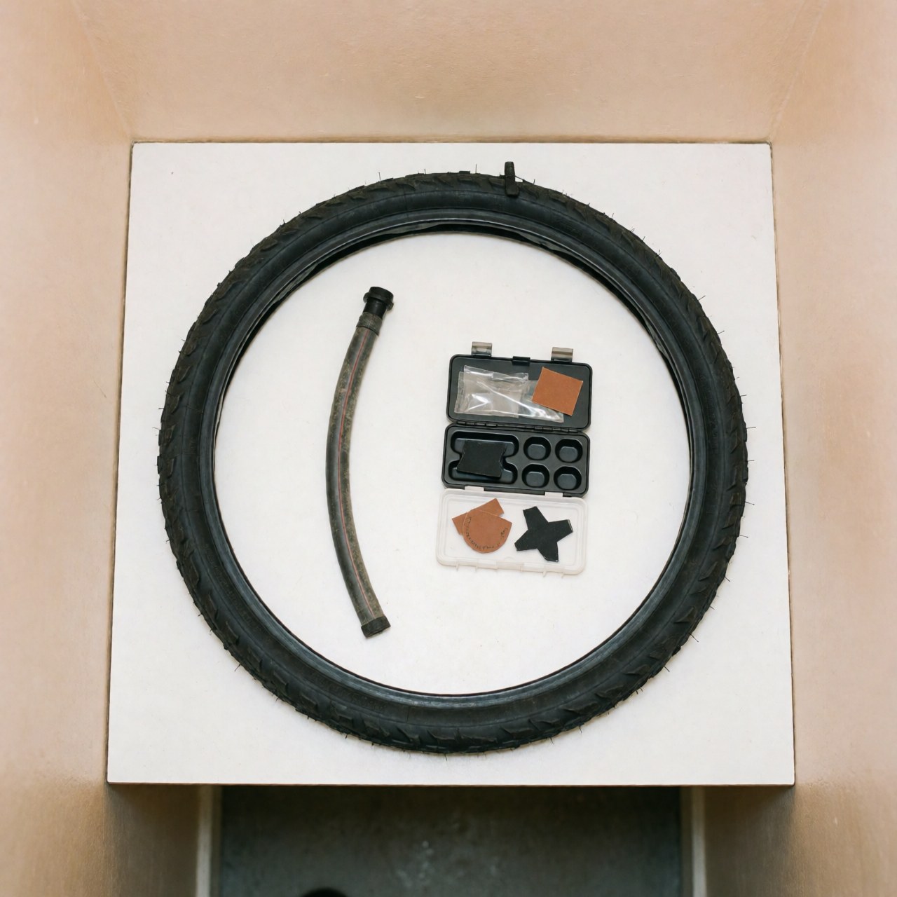 Pneu de vélo neuf accompagné d'un kit de réparation comprenant des patches et des outils sur fond blanc, idéal pour un atelier de bicyclettes.