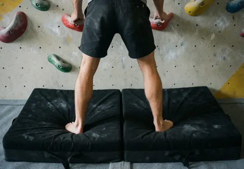 Escalade en intérieur avec mur et suspensions, un grimpeur sur des matelas noirs, lumière naturelle mettant en valeur la texture.