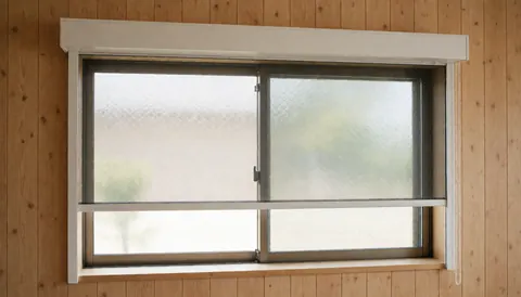 Fenêtre de maison équipée d'un store enrouleur blanc sur des murs en bois clair, baignée d'une lumière naturelle douce et idéale pour un service de réparation de fenêtres.