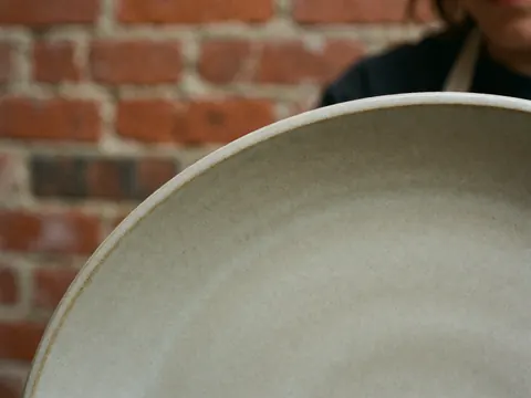 Assiette en terre cuite avec texture visible sur un fond de mur en briques rouges, mise au point sur le bord. Idéal pour illustrer un atelier de poterie.