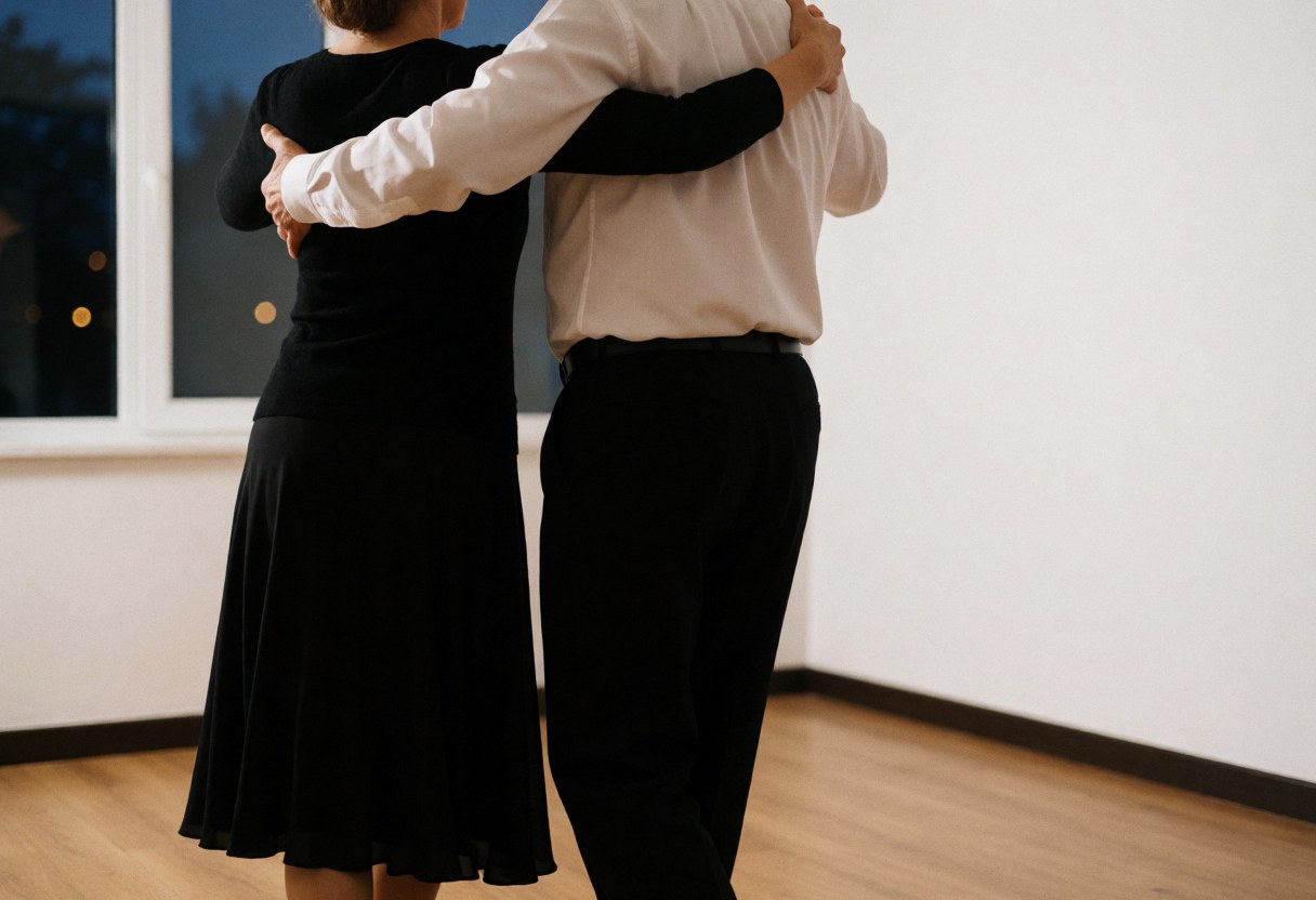 Vue arrière d'un couple en tenue de danse exécutant des pas de tango sur un sol en bois, baigné par une lumière douce provenant d'une fenêtre.