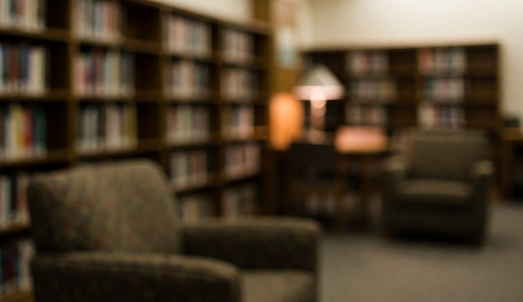 Fond de bibliothèque avec des étagères remplies de livres et des fauteuils rembourrés, éclairage doux et chaleureux, ambiance calme propice à l'étude.