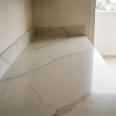 Plan de travail en quartz gris veiné dans une cuisine moderne avec murs beige, éclairage naturel diffus, surface polie et propre.