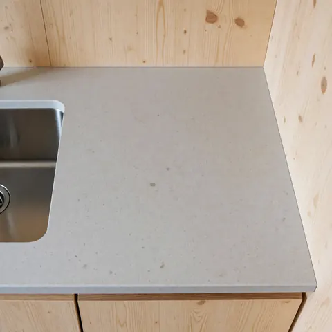 Vue de dessus d'un plan de travail en quartz gris intégrant un évier en acier inoxydable, sur fond de murs en bois clair. Design moderne et fonctionnel pour cuisine.