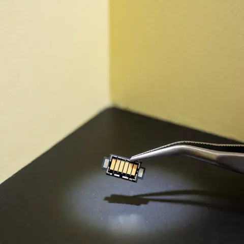 Connecteur usb-c doré tenu par des pinces sur fond sombre pour réparation de téléphones