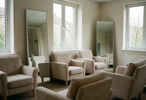 Salle d'attente avec des fauteuils confortables, des miroirs et des fenêtres laissant entrer la lumière naturelle, idéale pour les clients de piercing.