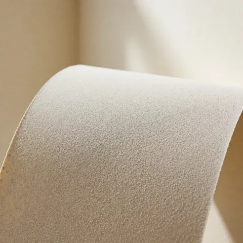 Feuille de papier de verre à grain fin avec texture visible, légèrement pliée, sur un fond beige doux, idéale pour la menuiserie et les finitions.