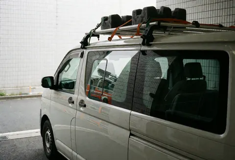 Fourgon blanc équipé d'un support sur le toit pour transporter du verre, stationné près d'un mur en grillage métallique avec des reflets sur les vitres.
