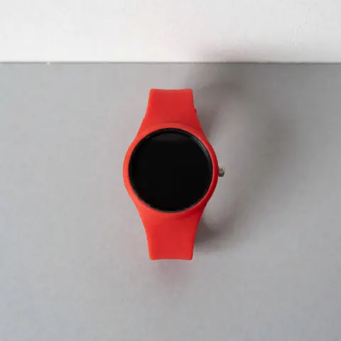 Montre de sport rouge avec bracelet en silicone et cadran noir, vue de dessus sur une surface grise neutre, idéale pour les boutiques de modernité.